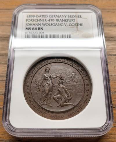 凡希社世界钱币微拍第三百二十一期 - 1899德国歌德诞辰150周年纪念铜章NGC-MS64，正面浮雕为拟人化的“诗歌女神”为歌德加冕的场景，环刻德语诗句“Nur die Sehnsucht bleibt, die ohne Dauer eilt”（唯有渴望永恒疾驰），背面雕刻歌德法兰克福出生地建筑实景。