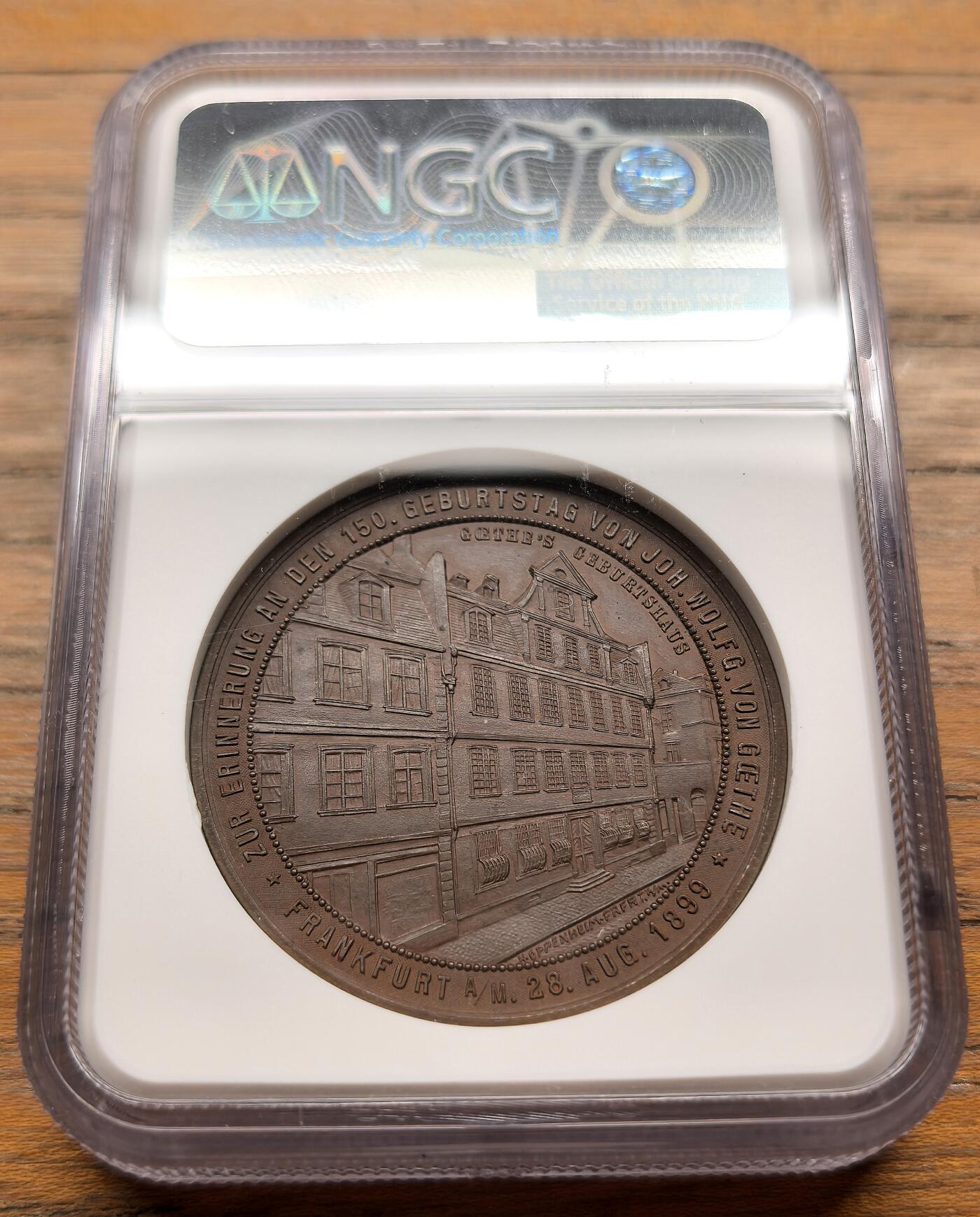 凡希社世界钱币微拍第三百二十一期 1899德国歌德诞辰150周年纪念铜章NGC-MS64，正面浮雕为拟人化的“诗歌女神”为歌德加冕的场景，环刻德语诗句“Nur die Sehnsucht bleibt, die ohne Dauer eilt”（唯有渴望永恒疾驰），背面雕刻歌德法兰克福出生地建筑实景。