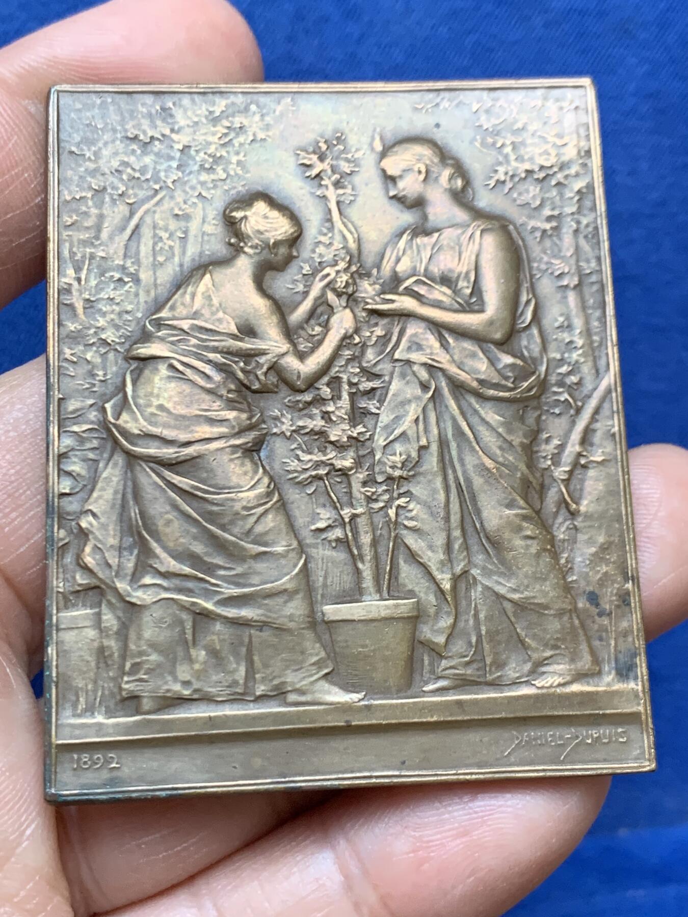 《竞宝斋》第470场 周日，周一，周二 3场连拍 （全场包邮）欢迎送拍 法国1892年园艺女神矩形大铜章，79.4克，61.5x48.5mm，大师Dupuis名作，Maier章牌目录122号。Dupuis也是名章“泉”“巢”系列的作者。双女神研究园艺种植，画面生动细致。铜光泛彩，状态上佳。