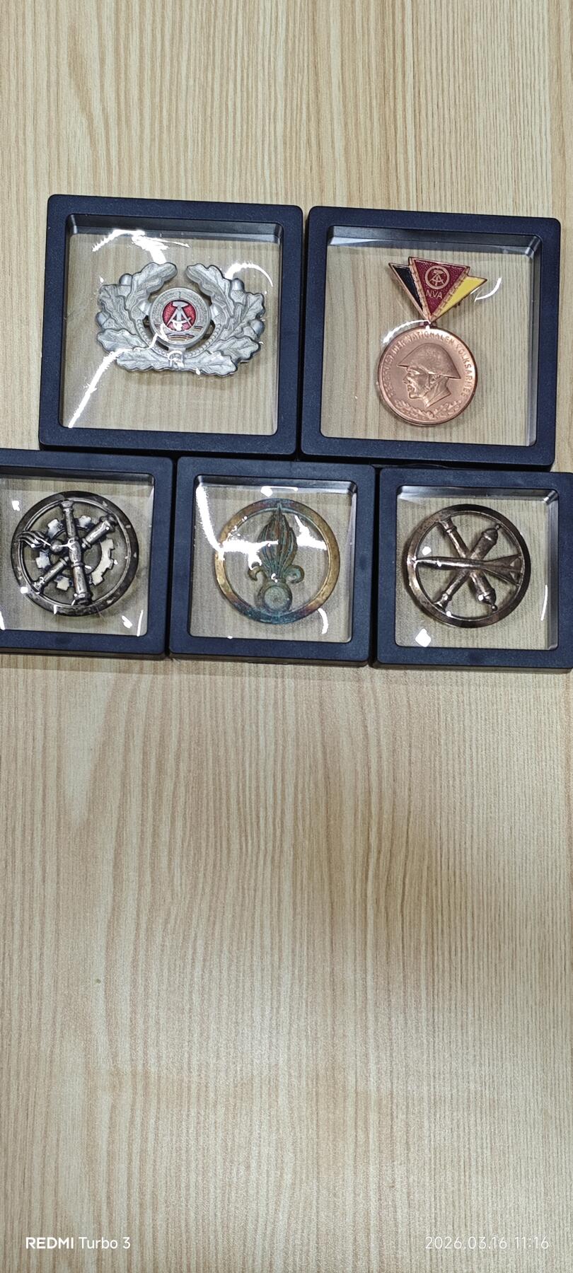 东德国家人民军（NVA）军官大檐帽徽、预备役铜质纪念章、工兵/炮兵兵种徽，搭配法国外籍军团鸢尾花贝雷帽徽，共5件。均为冷战时期原品，品相完好，细节清晰。适合军品收藏、历史研究或装饰展示。