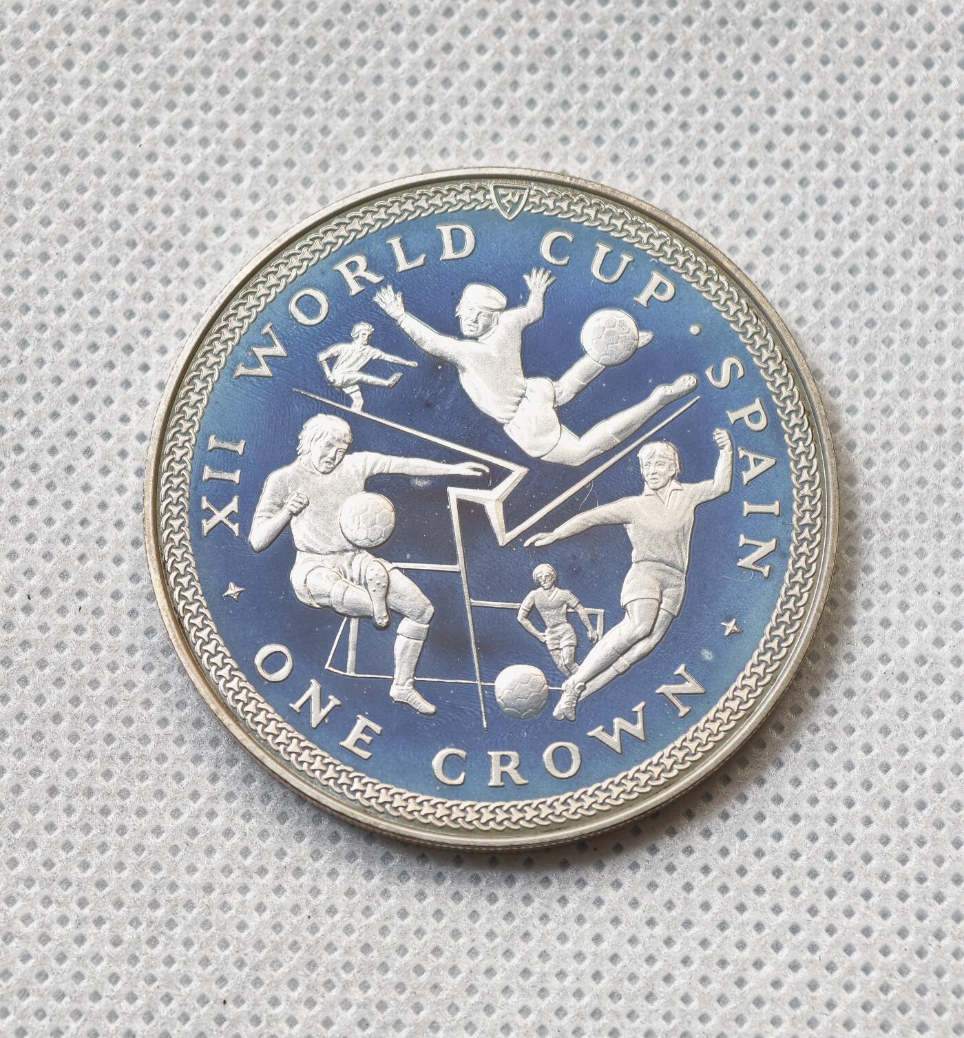 甄臻铺-世界币章拍卖（第55期），3月28日甄品场（直播拍卖）拍品征集中，送拍享返佣金等优惠多多 1982年马恩岛1克朗精制银币，FIFA世界杯主题，预热品种，发行量1.5万枚，28.5克925银