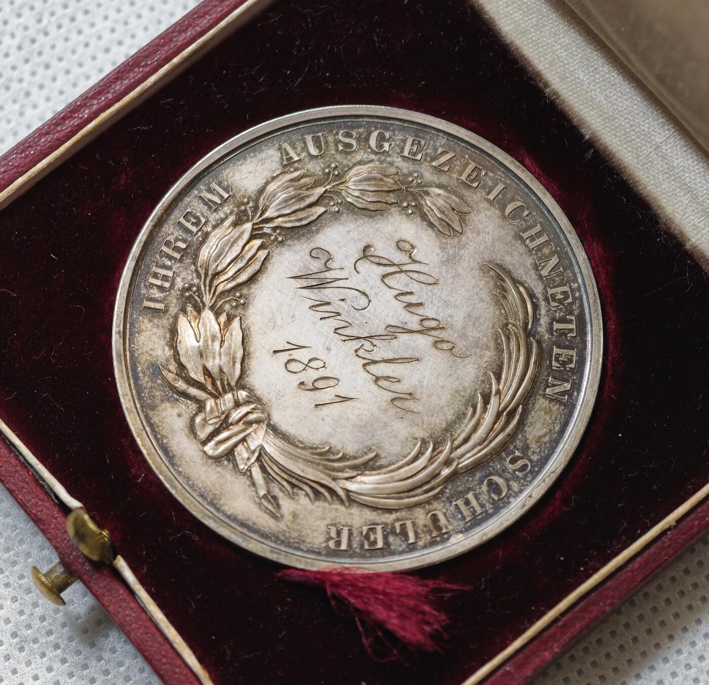 甄臻铺-世界币章拍卖（第55期），3月28日甄品场（直播拍卖）拍品征集中，送拍享返佣金等优惠多多 1891年奥地利维也纳商科学校颁发的银质奖章，直径43毫米，重21.9克，带原装皮盒。正面刻有“DIE WIENER GEMEINDE HANDELSCHULE”，背面“AUSGEZEICHNETEN SCHÜLER Hugo Winkler 1891”，环绕花环装饰，工艺精细，银质，包浆自然