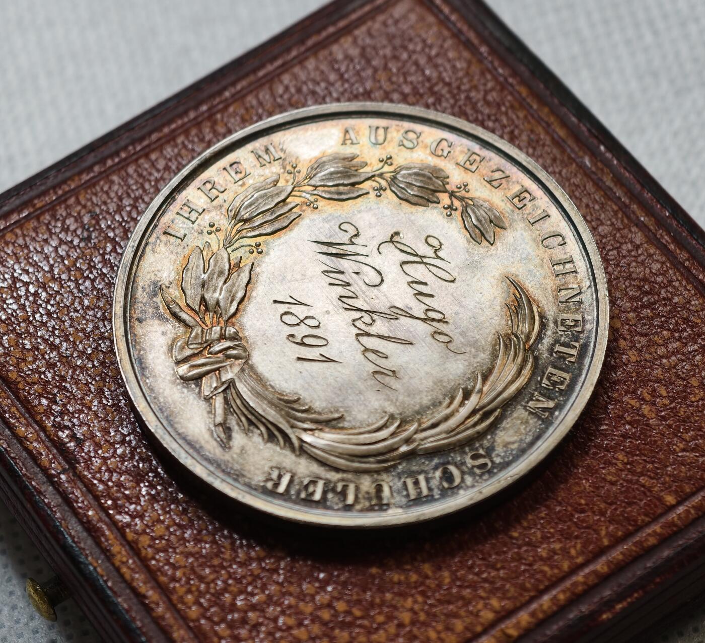 甄臻铺-世界币章拍卖（第55期），3月28日甄品场（直播拍卖）拍品征集中，送拍享返佣金等优惠多多 1891年奥地利维也纳商科学校颁发的银质奖章，直径43毫米，重21.9克，带原装皮盒。正面刻有“DIE WIENER GEMEINDE HANDELSCHULE”，背面“AUSGEZEICHNETEN SCHÜLER Hugo Winkler 1891”，环绕花环装饰，工艺精细，银质，包浆自然