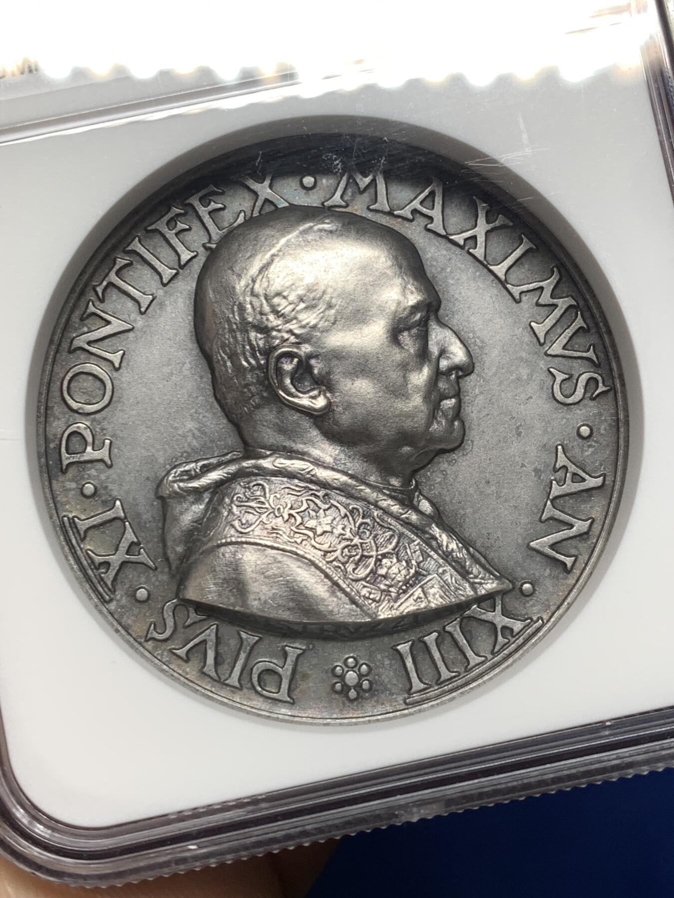 《竞宝斋》第474场 周日，周一 2场连拍 （全场包邮）欢迎送拍 NGC MS64 高分，加厚盒，稀少品种。梵蒂冈教皇庇护十一世于1934年发行的银质纪念章，由雕刻师A.Mistruzzi设计，用于纪念七位圣人的封圣仪式。纪念章正面为教皇左侧半身像，身着教宗礼服；背面描绘七位圣人立于云上，背景有十字架，铭文为拉丁语意“神圣救赎之年圆满结束”。该章发行了稀少，极具收藏价值。