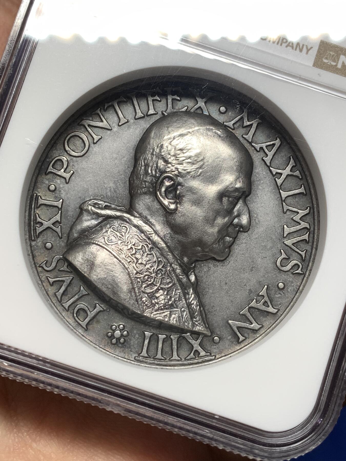《竞宝斋》第474场 周日，周一 2场连拍 （全场包邮）欢迎送拍 NGC MS64 高分，加厚盒，稀少品种。梵蒂冈教皇庇护十一世于1934年发行的银质纪念章，由雕刻师A.Mistruzzi设计，用于纪念七位圣人的封圣仪式。纪念章正面为教皇左侧半身像，身着教宗礼服；背面描绘七位圣人立于云上，背景有十字架，铭文为拉丁语意“神圣救赎之年圆满结束”。该章发行了稀少，极具收藏价值。