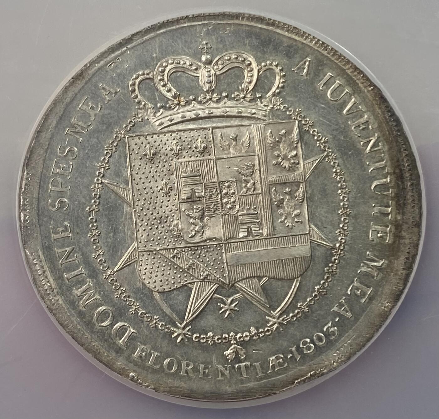 万国钱币拍卖第063期 NGC MS63 意大利托斯卡纳大公国1803年超大型10里拉大银币 正面为年幼的卡洛·路德维科和母亲摄政女王玛丽亚·路易萨，背面是含有法国波旁家族，拿破仑家族和美第奇家族等构成的华丽盾徽。此品种发行的首年，发行量9027枚且无后铸。此枚独特的地方在于币边比常见的更厚，尺寸较常规的更大，应是打制在了另外的币坯上，有试铸币的可能性。