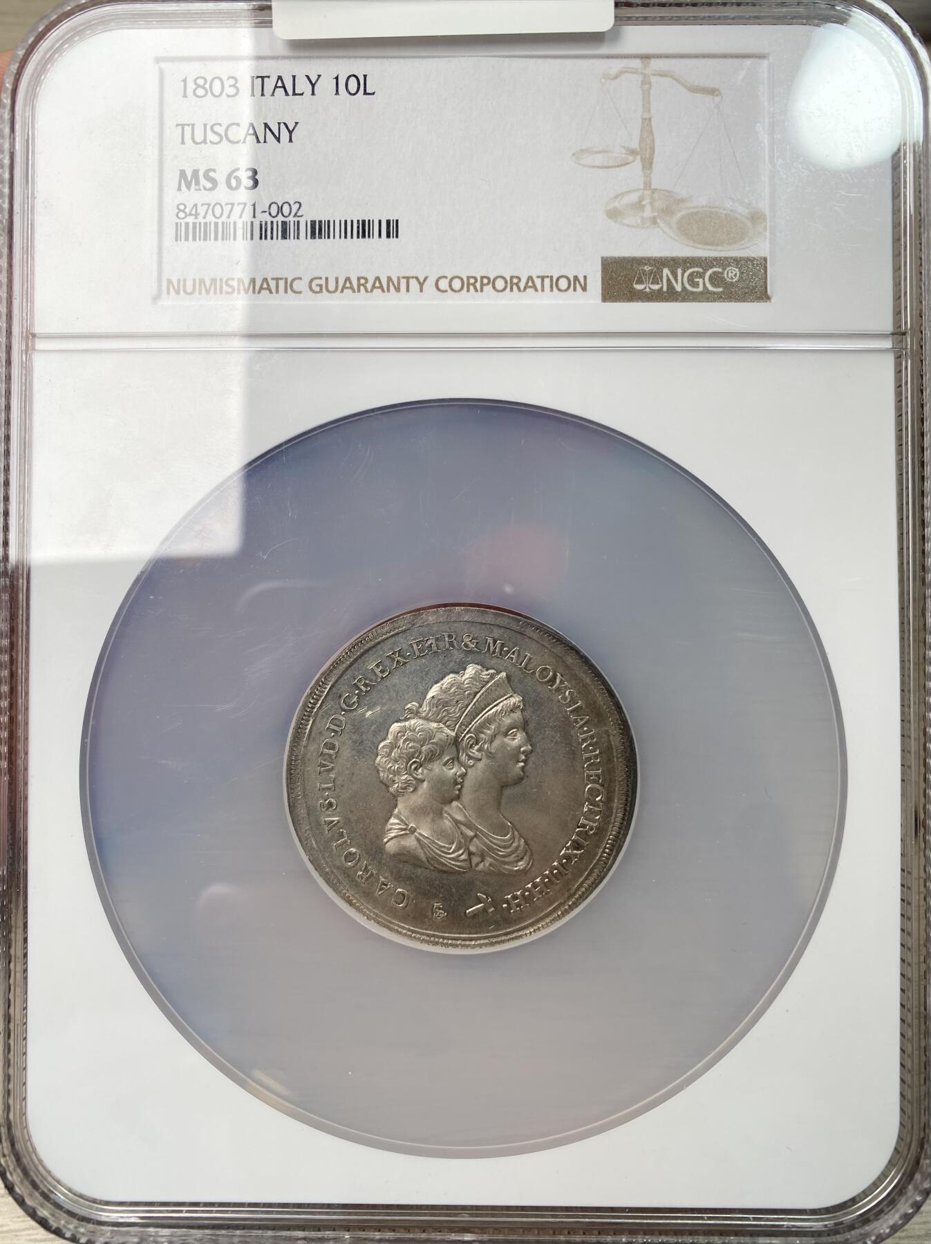 万国钱币拍卖第063期 NGC MS63 意大利托斯卡纳大公国1803年超大型10里拉大银币 正面为年幼的卡洛·路德维科和母亲摄政女王玛丽亚·路易萨，背面是含有法国波旁家族，拿破仑家族和美第奇家族等构成的华丽盾徽。此品种发行的首年，发行量9027枚且无后铸。此枚独特的地方在于币边比常见的更厚，尺寸较常规的更大，应是打制在了另外的币坯上，有试铸币的可能性。