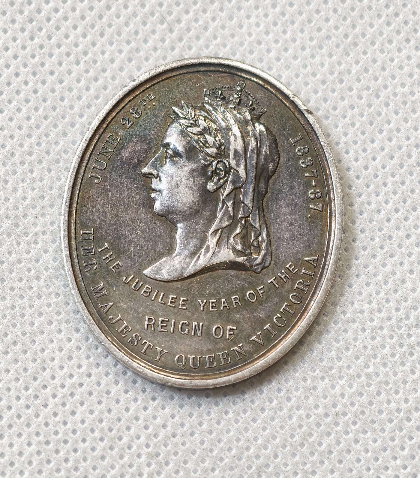 甄臻铺-世界币章拍卖（第56期），送拍享返佣金等优惠多多 1887年英国维多利亚女王登基50周年纪念获奖银章，由英国东南铁路公司颁发，椭圆形37.5x31.2毫米，重15克。正面维多利亚女王侧像，背面南东铁路徽章和人物肖像，见图，章顶部有貌似去吊环痕迹或许就是当时铸造时去浇口的痕迹，边缘有一处磕碰，其余完美。适合收藏或研究英国历史、铁路、维多利亚时期相关主题，非常稀少品种