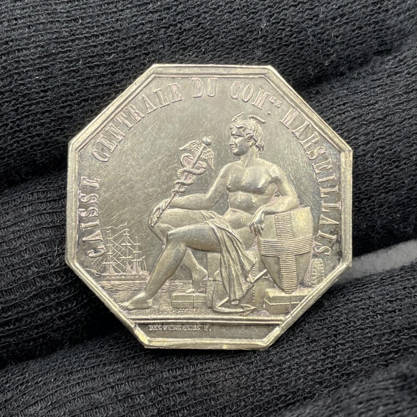 「木头集藏」“春启藏心”——章牌精品专场 1847年法国马赛商会中央金库八角银章，直径：30 mm，12.2 g，边铭：手指 ARGENT （1845-1860），少见八角。正面刻画商业之神赫尔墨斯的坐姿像，他手持双蛇杖（商业与贸易的象征），身旁有船锚、商船、盾牌（马赛市徽十字盾）与货箱，呼应马赛作为地中海商业港口的身份