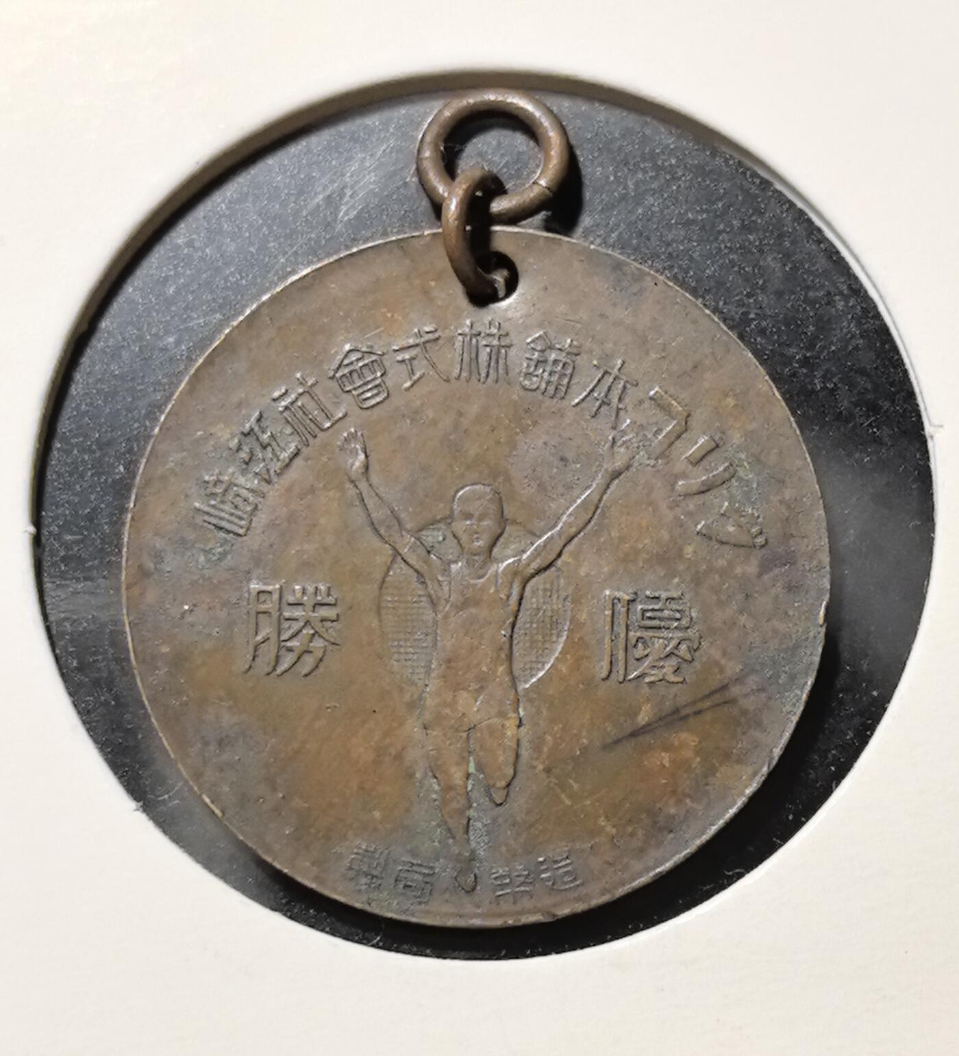 外国优质老铜币银币苏联纪念章，每周六晚九点倒数截拍，满百包邮可寄存，持续收拍 优胜铜质纪念章直径22.6mm重3克，正面为戎装人物肖像，背面是振臂奔跑的运动员形象与 “優勝” 字样，搭配日文商号铭文，是近代日本体育赛事与商业文化的实物见证，包浆自然，兼具历史与收藏价值。