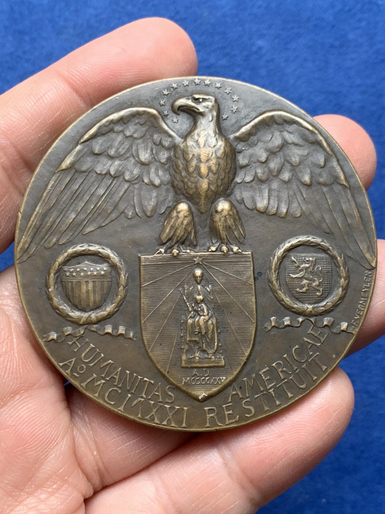 《竞宝斋》第475场 周日，周一 2场连拍 （全场包邮）欢迎送拍 1921年美国铸造比利时鲁汶大学图书馆纪念章，该纪念章英国帝国战争博物馆有藏，极具历史背景和意义，值得收藏品鉴，少见品。正面文字：（拉丁语，意为“美国于1921年恢复人道精神”）。图案：美国白头鹰立于盾徽之上，盾徽内是圣母与圣子像，两侧分别嵌有美国国旗纹章和比利时雄狮纹章，象征美比两国的联结。背面：（拉丁语，意为“1914年被德国军队焚毁的鲁汶大学图书馆”）。图案：刻画鲁汶大学图书馆内部的罗马式拱