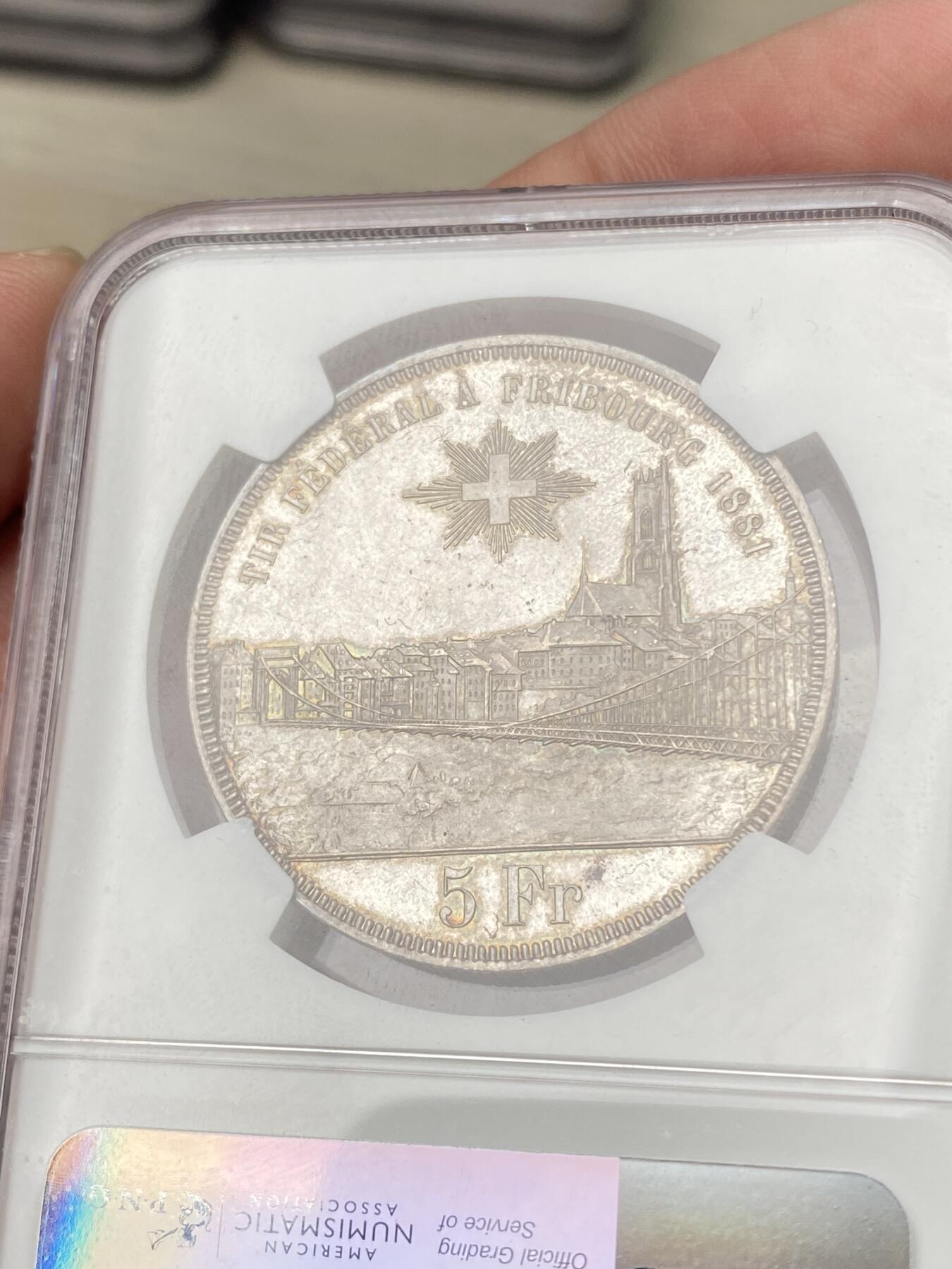 万国钱币拍卖第064期 NGC MS64 1881年瑞士弗里堡射击节经典城市景观5法郎 广受欢迎的瑞射景观系列 银霜转光香槟金淡彩环绕 极其舒适的收藏级品质