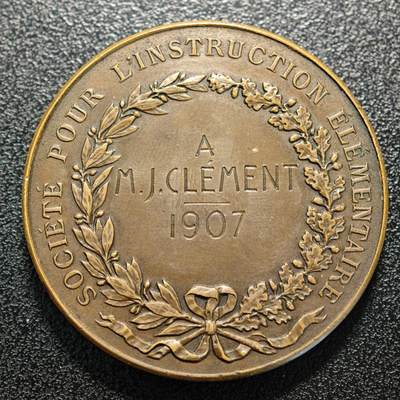 【德藏】世界币章拍卖第170期（拍品征集中~欢迎藏友联系） 1907年 法国初级教育协会纪念铜章，1815年版本，正面是三个坐着的小孩子正在书写板上做记录，站着天使指着墙上挂着的三块中间的牌子正在教导他们；背面是月桂和橡木枝组成的花环和铭文 直径约：41.2mm；重约：37.6g