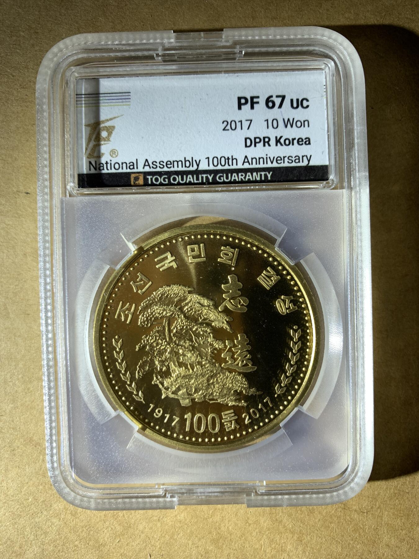 【礼羽收藏】🌏世界钱币拍卖第132期 朝鲜2017年发行的10元纪念币，纪念最高人民会议成立100周年，评级PF 67 UC（精制币，镜面深打67分）。材质是铜镍合金，金黄色调，正面有“志远”和松树图案。