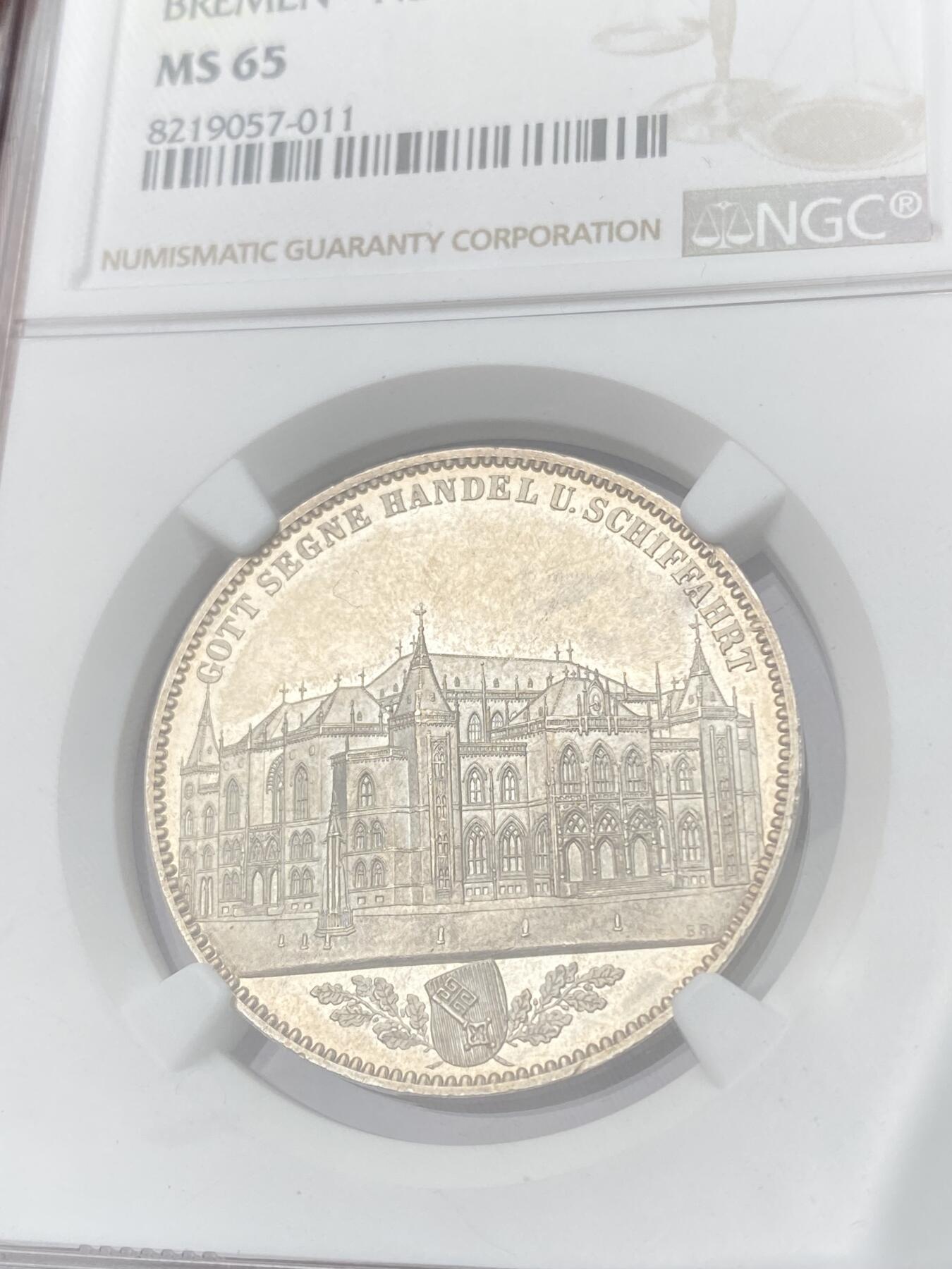 万国钱币拍卖第064期 NGC MS65 1864年不来梅证券交易所泰勒 名誉品种，来自汉诺威厂的顶级工艺，双面香槟金彩裹身霜感极强高点堪称完美，仅单年发行5000枚，BU品质极其罕见。不来梅自由市为纪念该新交易所于1864年11月5日开业而发行，正面为交易所景观，下方为饰以橡树枝叶的不来梅市徽，上方刊德文“上帝保佑贸易与航运”这座美丽的新哥特风格建筑在1943年毁于战火，庆幸的是还能在此币上欣赏她的美丽。