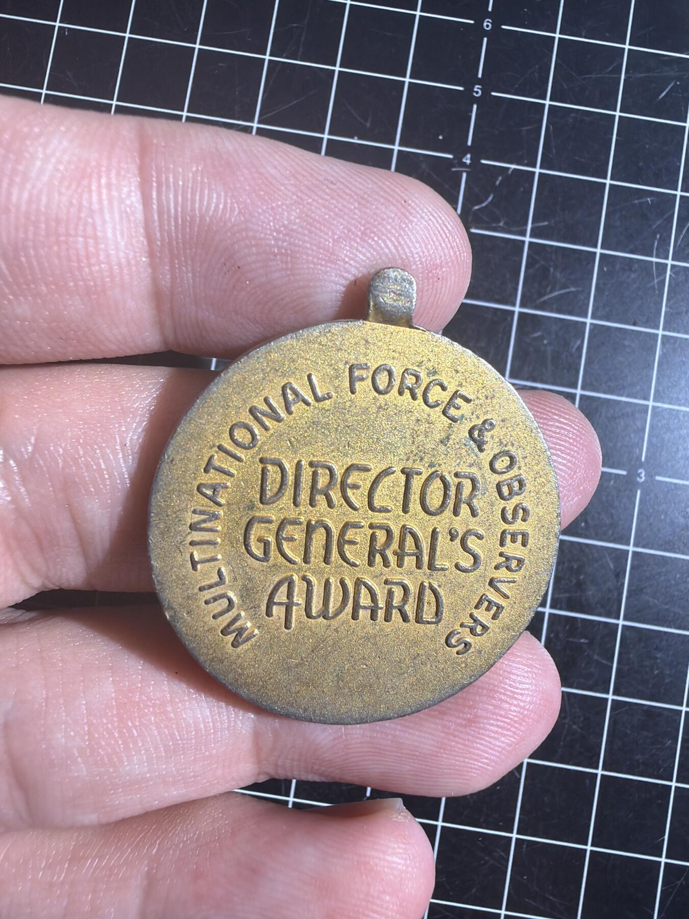 古冰库章牌勋赏收藏0起拍卖 联合国多国部队纪念章，铜质徽章挂件，直径约3.5cm，厚实有分量。正面刻“UNITED IN SERVICE FOR PEACE”，背面“MULTINATIONAL FORCE & OBSERVERS DIRECTOR GENERAL'S AWARD