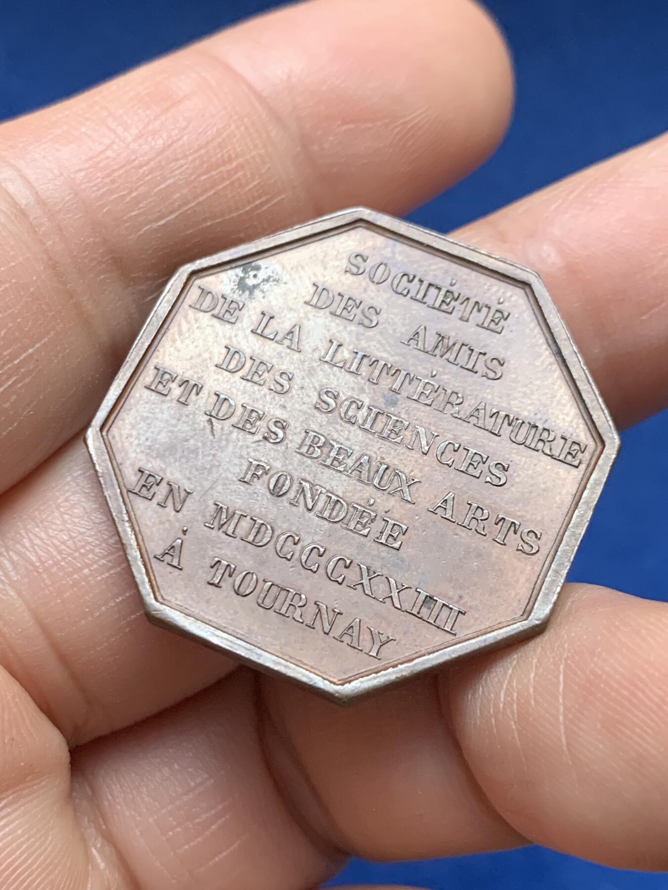 《竞宝斋》第478场 周日，周一 2场连拍 （全场包邮）欢迎送拍 1823年比利时图尔奈文学、科学与美术之友协会八角形纪念章，存世量较少，正面刻有里拉琴（代表文学艺术），月桂枝（象征荣誉），祭坛式纹饰搭配放射状星芒。19世纪新古典艺术主义，具有较高的收藏价值。直径：31.3mm，重：11.55g