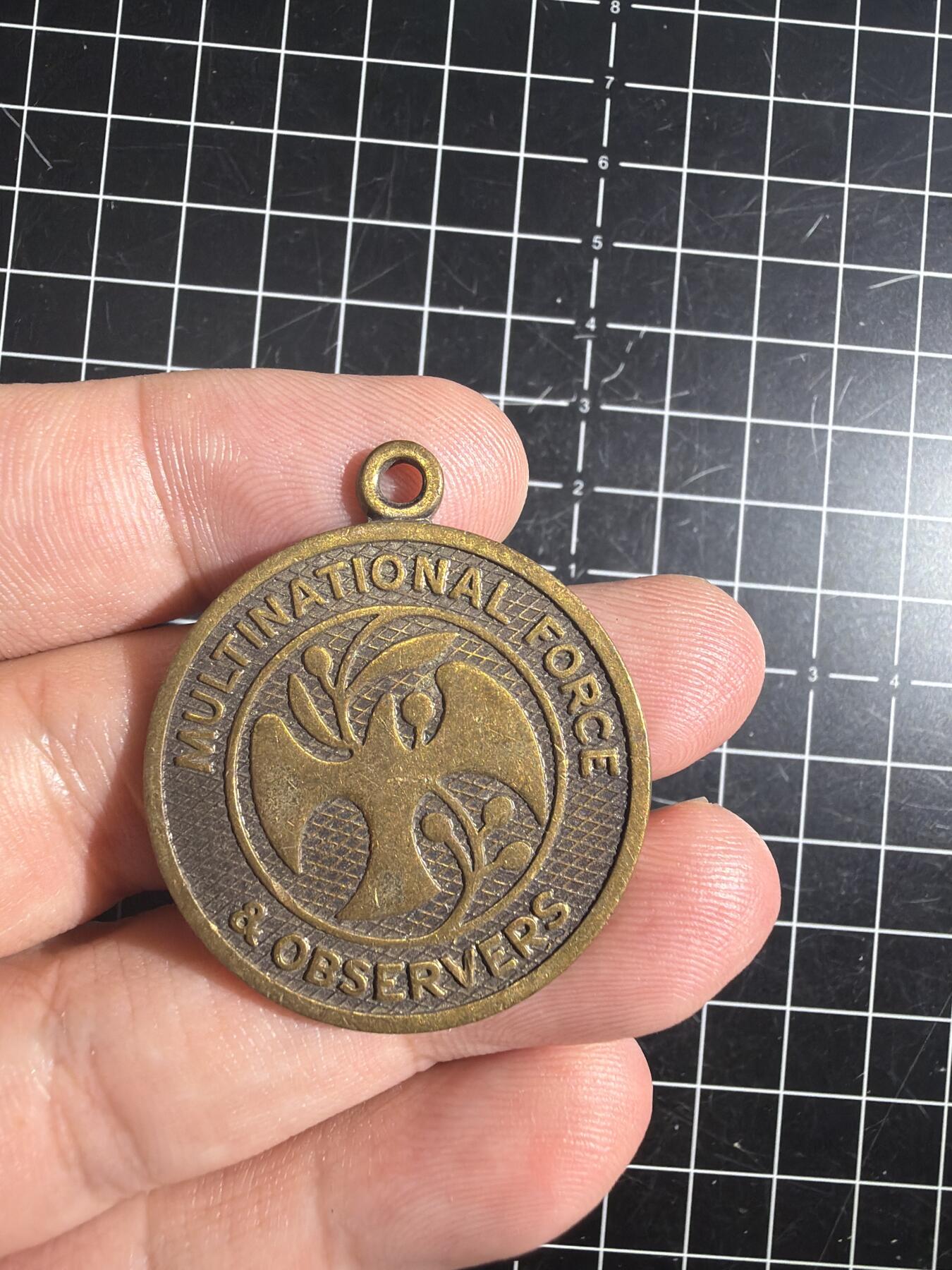 古冰库章牌勋赏收藏0起拍卖 联合国多国部队纪念章，铜质徽章挂件，直径约3.5cm，厚实有分量。正面刻“UNITED IN SERVICE FOR PEACE”，背面“MULTINATIONAL FORCE & OBSERVERS DIRECTOR GENERAL'S AWARD