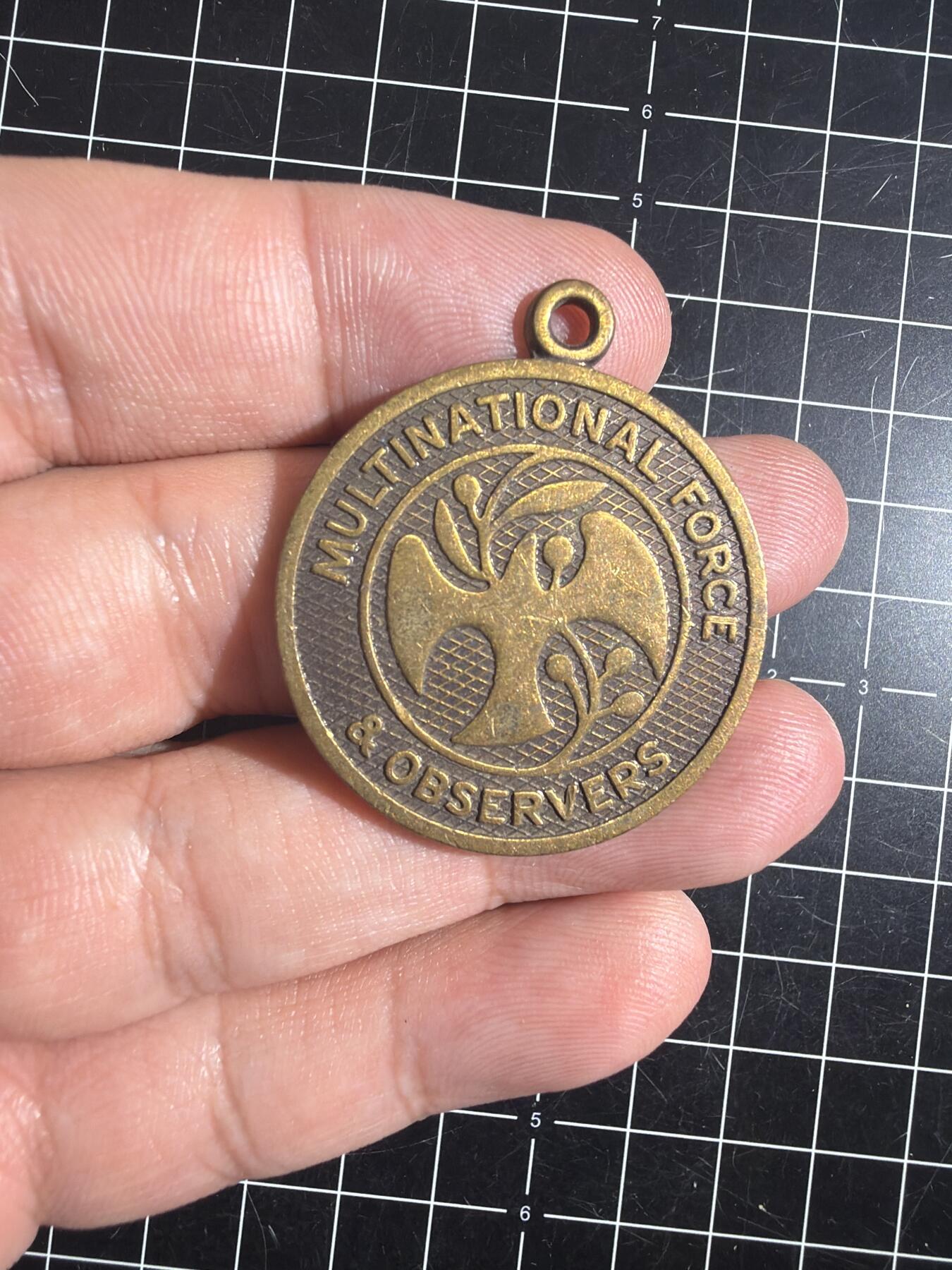 古冰库章牌勋赏收藏0起拍卖 联合国多国部队纪念章，铜质徽章挂件，直径约3.5cm，厚实有分量。正面刻“UNITED IN SERVICE FOR PEACE”，背面“MULTINATIONAL FORCE & OBSERVERS DIRECTOR GENERAL'S AWARD