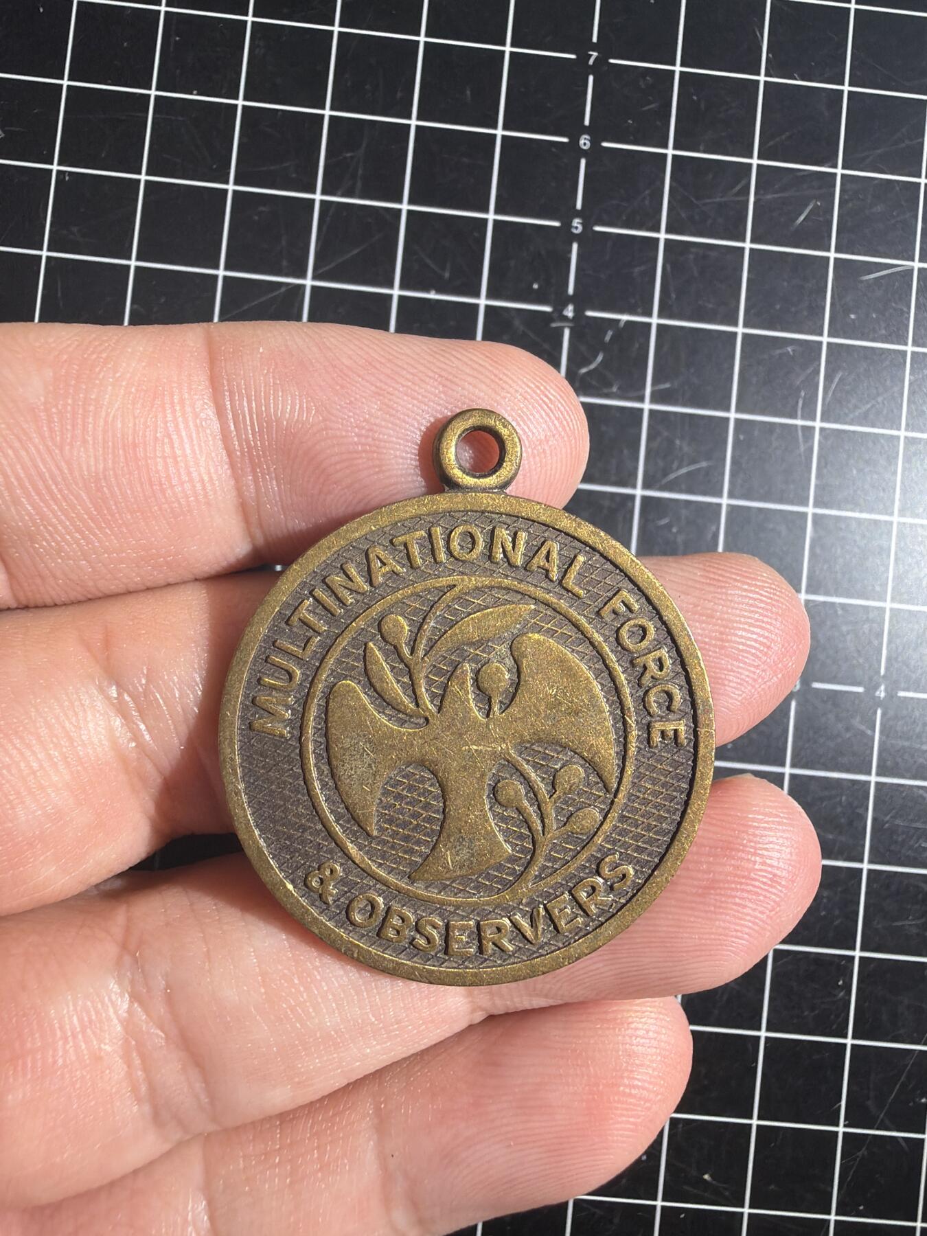 古冰库章牌勋赏收藏0起拍卖 联合国多国部队纪念章，铜质徽章挂件，直径约3.5cm，厚实有分量。正面刻“UNITED IN SERVICE FOR PEACE”，背面“MULTINATIONAL FORCE & OBSERVERS DIRECTOR GENERAL'S AWARD