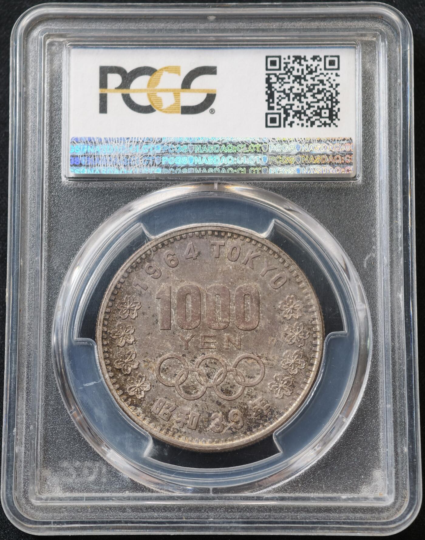 甄臻铺-世界币章拍卖（第59期），甄品场拍品征集中，送拍享返佣金等优惠多多 PCGS-MS66，日本1964年奥运银币，日本大奥1000日元，带官网高清大图，红绿蓝五彩渐变。盒子正面一处裂纹，表面光滑不影响密封
