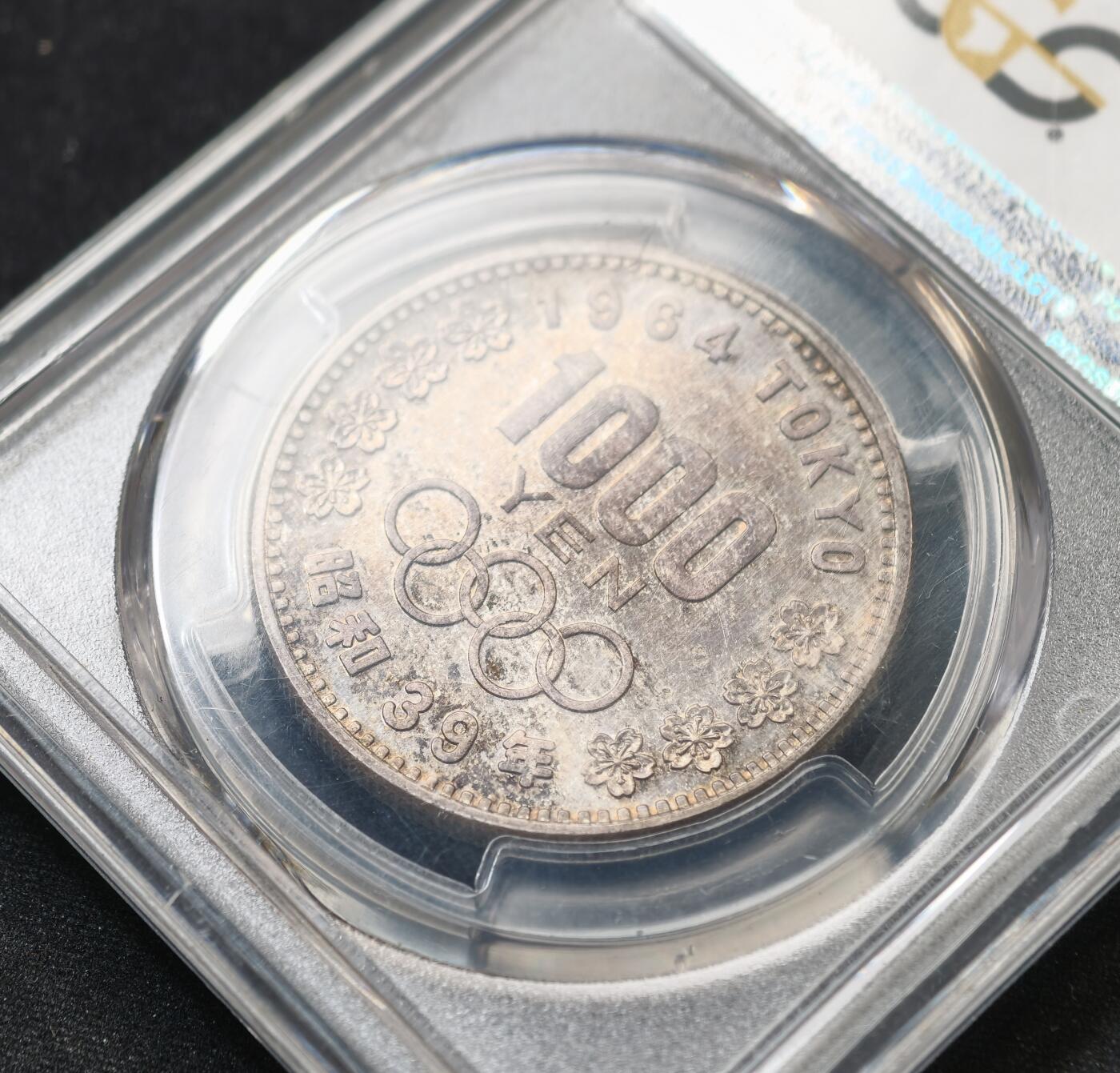 甄臻铺-世界币章拍卖（第59期），甄品场拍品征集中，送拍享返佣金等优惠多多 PCGS-MS66，日本1964年奥运银币，日本大奥1000日元，带官网高清大图，红绿蓝五彩渐变。盒子正面一处裂纹，表面光滑不影响密封