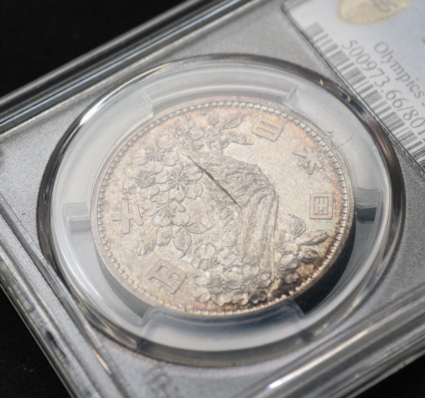 甄臻铺-世界币章拍卖（第59期），甄品场拍品征集中，送拍享返佣金等优惠多多 PCGS-MS66，日本1964年奥运银币，日本大奥1000日元，带官网高清大图，红绿蓝五彩渐变。盒子正面一处裂纹，表面光滑不影响密封