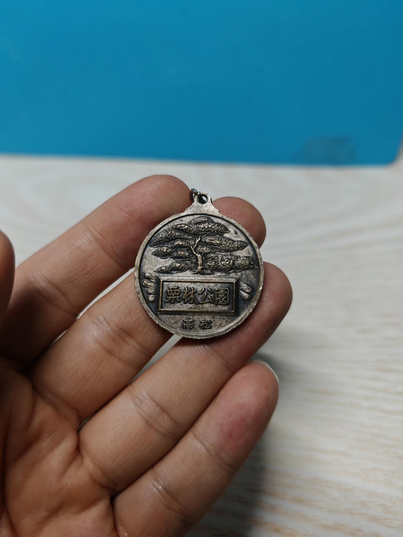 日本香川县高松市栗林公园观光纪念章，铜质，直径约32.3mm，正面“栗林公园 高松”，以及栗林公园最标志性的元素——园内有超过1400棵精心修剪的松树，背面公园风景浮雕，整体成色还可以，有正常使用痕迹，无明显磕碰。适合钱币、纪念章收藏