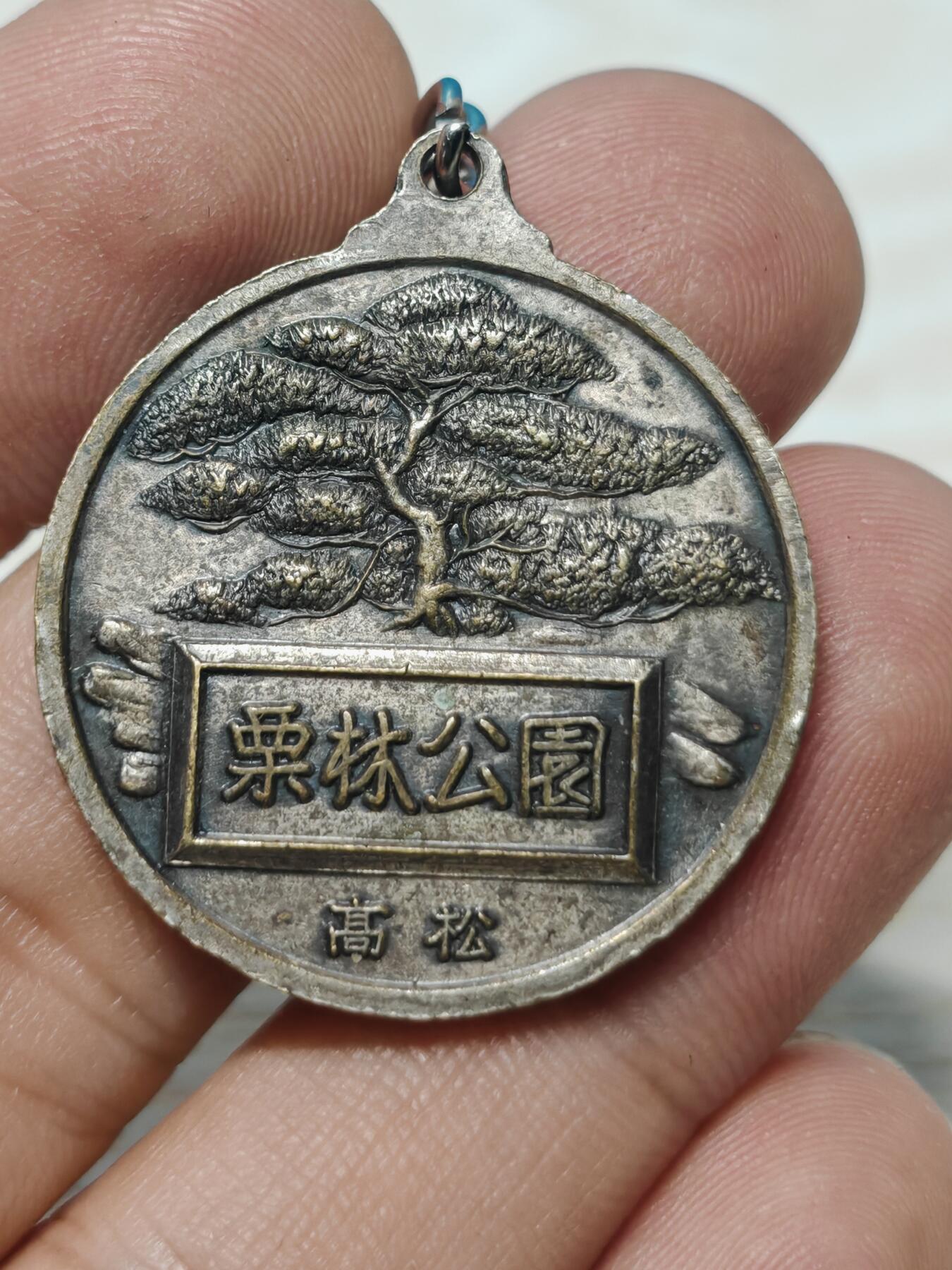 日本香川县高松市栗林公园观光纪念章，铜质，直径约32.3mm，正面“栗林公园 高松”，以及栗林公园最标志性的元素——园内有超过1400棵精心修剪的松树，背面公园风景浮雕，整体成色还可以，有正常使用痕迹，无明显磕碰。适合钱币、纪念章收藏