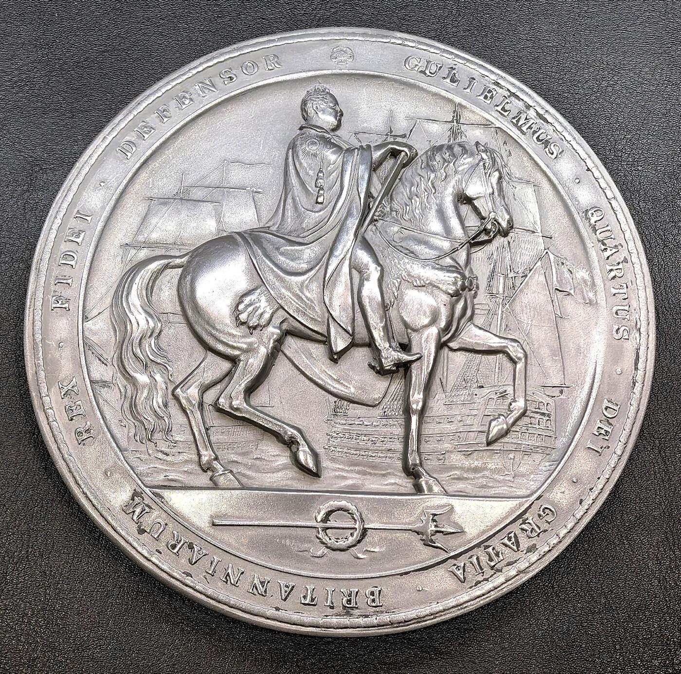 凡希社世界钱币微拍第三百二十二期 十九世纪英国纪念威廉四世高浮雕白色金属超大挂章，直径150mm，重387g，身着长袍的国王威廉四世骑马出征形象，马匹昂首前视，国王手持权杖，姿态威严，后方可见帆船舰队轮廓，契合威廉四世作为“海军国王”的身份背景，底部的花环与三叉戟进一步强化了海权与王权的关联。整体保存状态上佳。