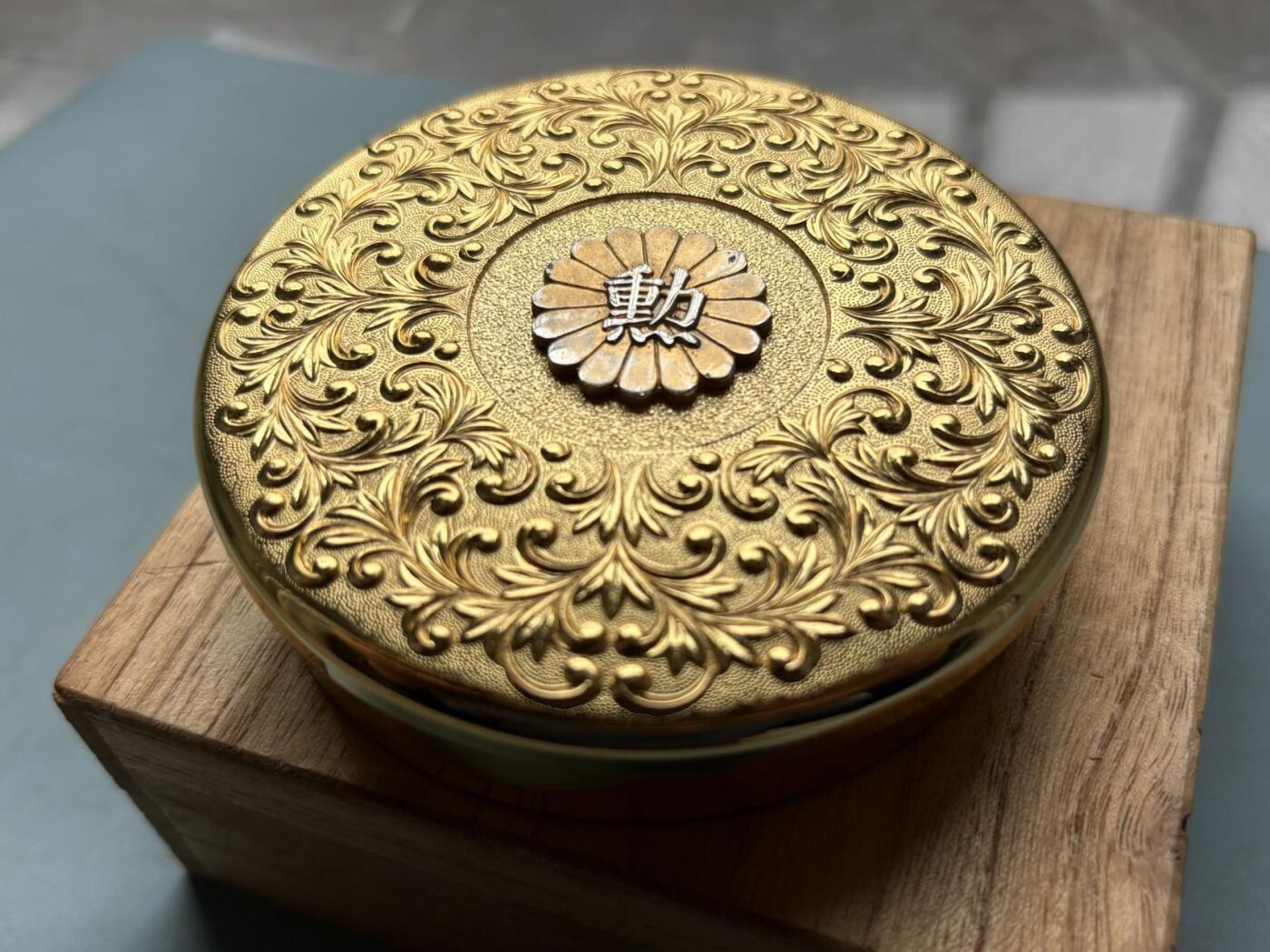 盛世勋华——号角文化勋章邮票专场拍卖第314期 日本昭和48年（1973年）勋四等瑞宝章受章纪念金盒，原桐木盒带受章人吉冈一二手书铭文，满工唐草纹錾刻，中心菊纹嵌银“勋”字，工艺精湛，大尺寸