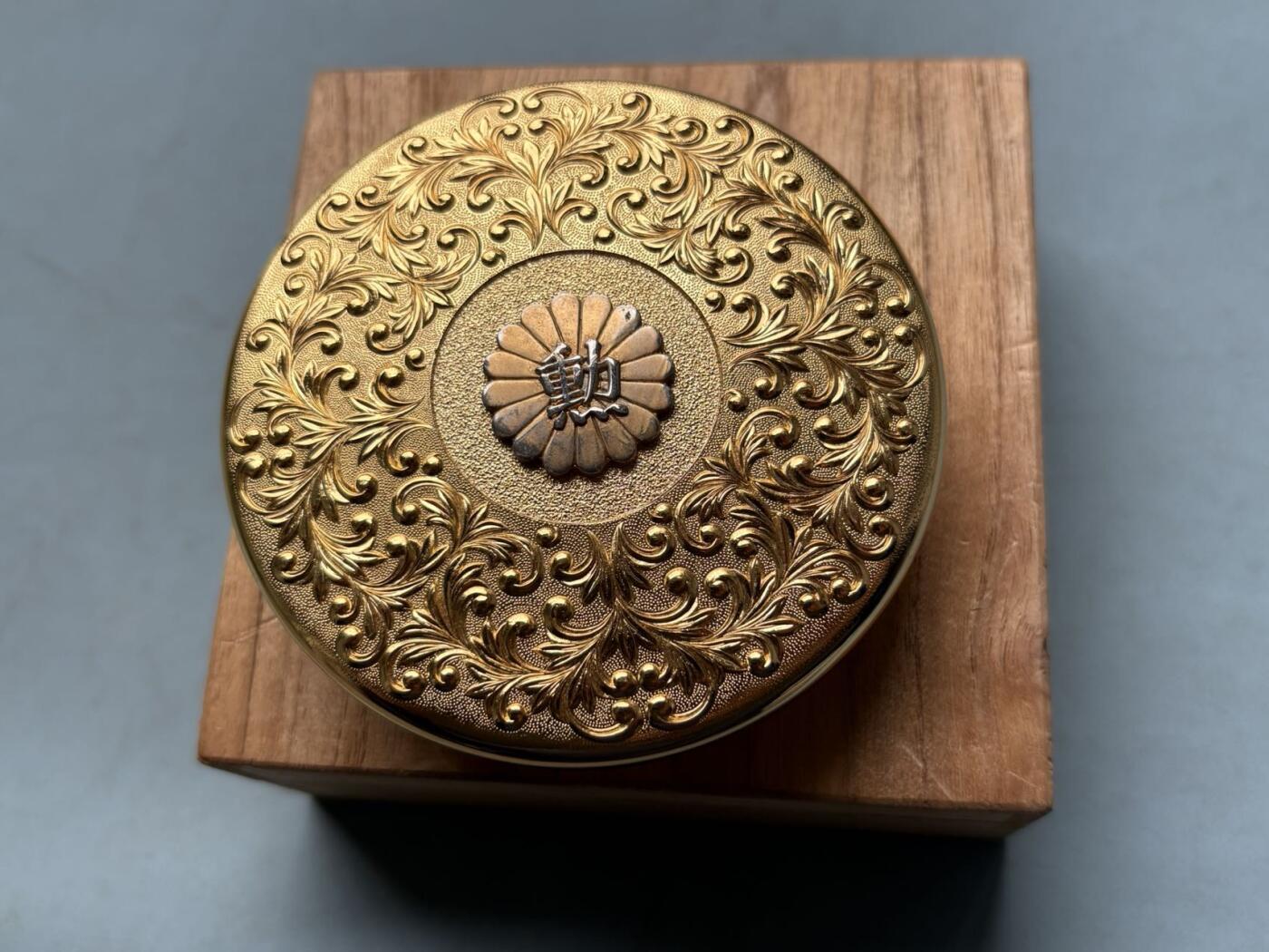 盛世勋华——号角文化勋章邮票专场拍卖第314期 日本昭和48年（1973年）勋四等瑞宝章受章纪念金盒，原桐木盒带受章人吉冈一二手书铭文，满工唐草纹錾刻，中心菊纹嵌银“勋”字，工艺精湛，大尺寸