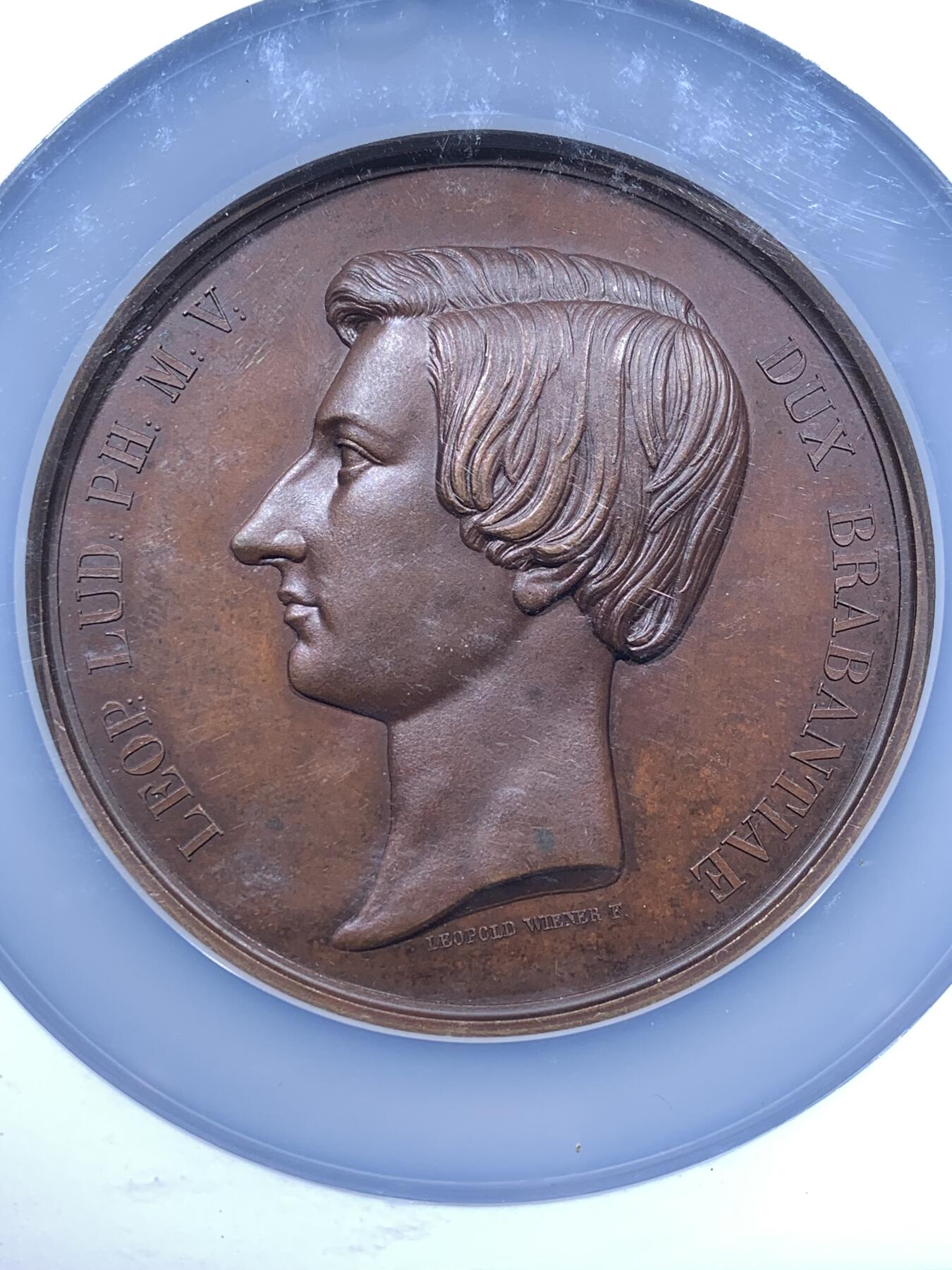 《竞宝斋》第481场 周日，周一 2场连拍 （全场包邮）20级店铺 欢迎送拍 NGC MS64BN 比利时1853年利奥波德二世成年宣誓制造大规格铜章，由著名章牌雕刻师Leopold Wiener设计制作（大名定鼎鼎），该章是王室章牌中的经典藏品。英国皇家收藏、法国国家图书馆、澳大利亚维多利亚馆均有收藏。可见盖该章的历史性和收藏价值。双面高浮雕，巧克力包浆，直径：75mm，重：175g，加大加厚盒装。