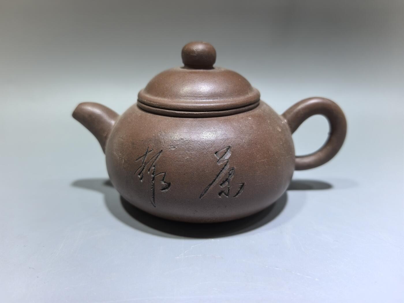 旧藏紫砂老壶，取原矿紫泥为料，泥色温润沉穆，包浆由岁月与茶汤浸润而成，光气内敛，尽显旧物之美。壶型饱满敦实，盖钮圆润如珠，壶流短直流畅，壶把圈握趁手，整体线条简练流畅，颇具传统工夫茶器的朴雅气质。高约6.0cm长约10.5cm