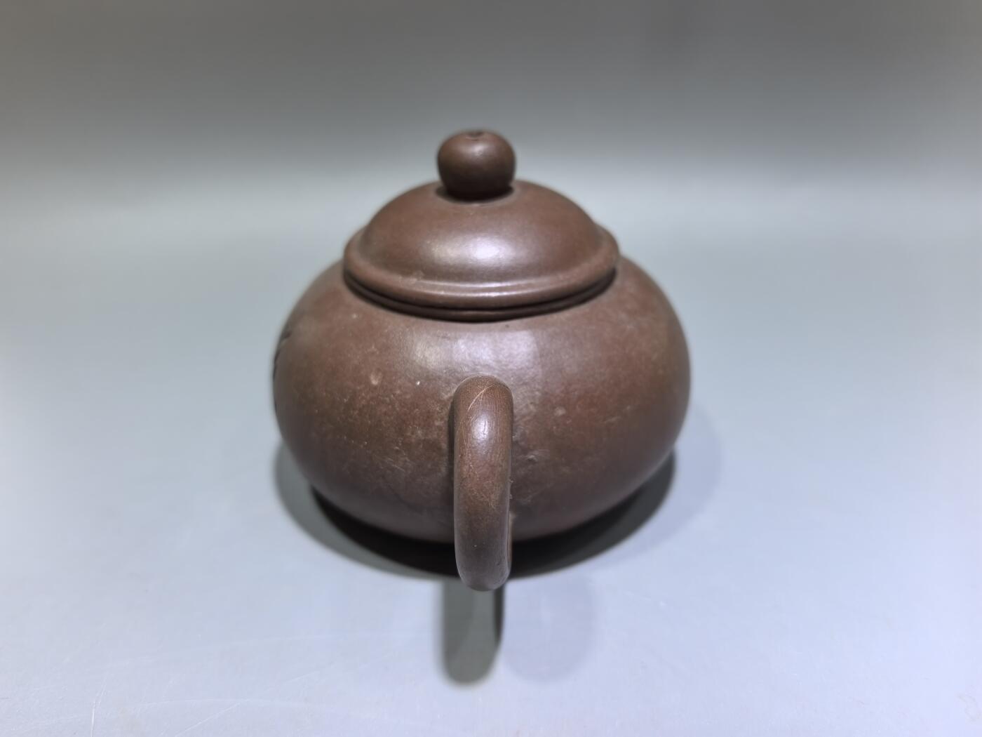 旧藏紫砂老壶，取原矿紫泥为料，泥色温润沉穆，包浆由岁月与茶汤浸润而成，光气内敛，尽显旧物之美。壶型饱满敦实，盖钮圆润如珠，壶流短直流畅，壶把圈握趁手，整体线条简练流畅，颇具传统工夫茶器的朴雅气质。高约6.0cm长约10.5cm