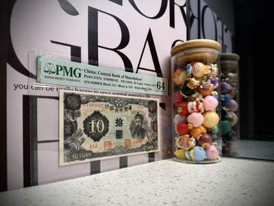 （自动截拍）PMG评级民国纸币专拍第20260424期，全场包邮 【乾奕收藏】出民国33年1944年满洲中央银行财神像圆，财神赵公明图案，丙券长号码版本，美国PMG64分