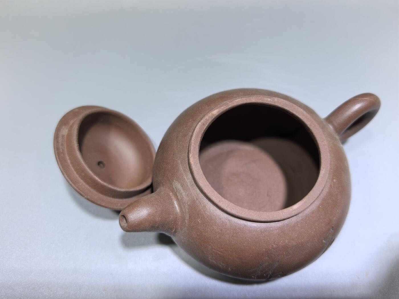 旧藏紫砂老壶，取原矿紫泥为料，泥色温润沉穆，包浆由岁月与茶汤浸润而成，光气内敛，尽显旧物之美。壶型饱满敦实，盖钮圆润如珠，壶流短直流畅，壶把圈握趁手，整体线条简练流畅，颇具传统工夫茶器的朴雅气质。高约6.0cm长约10.5cm