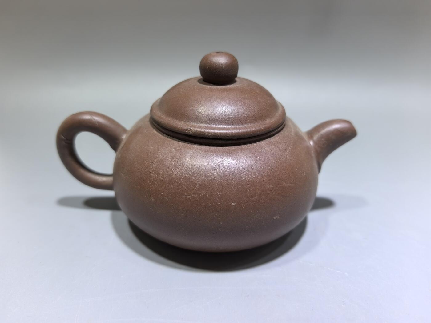 旧藏紫砂老壶，取原矿紫泥为料，泥色温润沉穆，包浆由岁月与茶汤浸润而成，光气内敛，尽显旧物之美。壶型饱满敦实，盖钮圆润如珠，壶流短直流畅，壶把圈握趁手，整体线条简练流畅，颇具传统工夫茶器的朴雅气质。高约6.0cm长约10.5cm