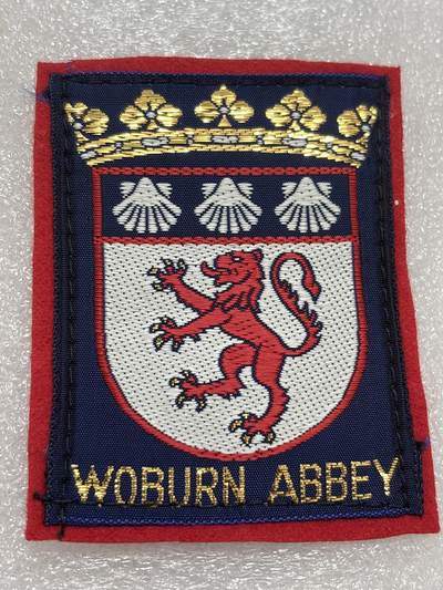 文馨钱币收藏第 302 场，国外回流老铜币，中东阿拉伯地区，拉美等国货币，30 号 1 号二连拍，长期接代拍业务，预计 4 月 4-5 号发货 沃本修道院的刺绣徽章  顶部有一顶金色的王冠/公爵冠 •  盾章上半部分有三只白色的扇贝形图案 •  盾章下半部分有一只红色的跃立狮子  沃本修道院位于英国英格兰贝德福德郡，是贝德福德公爵（Duke of Bedford）的家族宅邸。这座庄园始建于1145年，原为西多会修道院，后于16世纪解散修道院时期被赐予罗素家族，改建为私人宅邸。修道院及其周围的沃本野生动物园