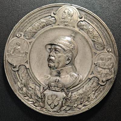 【德藏】世界币章拍卖第175期 - 1871年德意志帝国统一大型白色金属纪念章，直径约100.3mm，重量约259.7g，高浮雕工艺，普鲁士国王暨德意志皇帝威廉一世戎装肖像，环饰德法战争与德意志统一历史场景，背面三皇肖像与帝国鹰徽图案，德意志帝国官方纪念艺术章